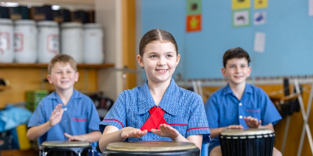 Three students playing drums with their hands.