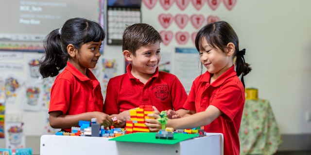 Three students in red shirts in a classroom playing with LEGO.